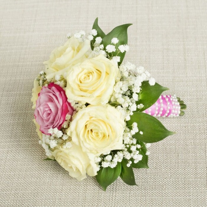 Evoking the elegant yet lively character of Highgate, this compact floral bouquet is showcased from above against a soft, canvas-like background-a vision crafted by local hands for a truly special event. At the bouquet's heart, five or six creamy-white roses exude freshness, their petals not yet fully opened, symbolising hope and new adventures ahead. Just off-centre, a striking fuchsia-pink rose draws instant attention, its bold vibrancy recalling the colourful window boxes seen along Highgate High Street. Delicate sprays of baby's breath (gypsophila) drift throughout the design, introducing lightness and movement and contrasting with the richness of the rose petals. A cluster of deep green leaves around the base brings in the woodland feel so beloved by residents who frequent the paths of Queen's Wood or Waterlow Park. The bouquet's handle is finished in a luxurious, fuchsia-pink satin ribbon, intricately coiled with a luminous string of pearls, bringing a refined, classic accent to the arrangement. Resting on a softly woven textile, this bouquet shines with romantic intention and expert technique, making it particularly suited for articles or occasions that celebrate bridal traditions, Highgate nuptials, or the art of sophisticated floral design.