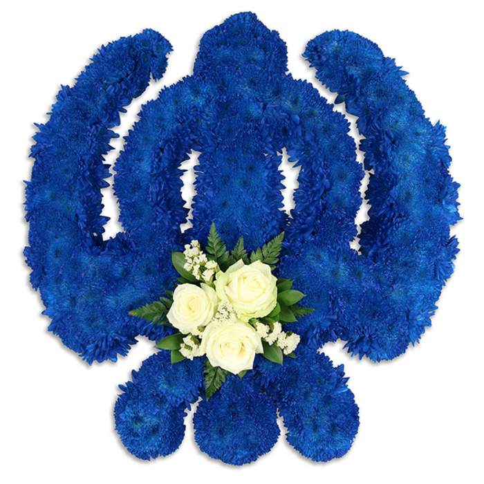 An imposing, carefully balanced floral Khanda symbol fills the viewer's field of vision, set against a pristine white background that allows every blue petal to stand out. The chakkar, central sword and twin kirpans are all delineated by an unbroken sea of royal blue chrysanthemums, arranged so densely that the underlying frame is completely hidden. The petals cluster together to create a luxuriously thick, almost velvety surface, with small variations in tone giving the blue depth and character, like the evening sky seen from Highgate Hill. The lines of the emblem are crisp and confident, showing the hand of an experienced florist who has shaped the flowers into smooth arcs and clean edges that honour the sacred geometry of the Sikh Khanda. At the lower centre of the design, a contrasting motif softens the strong symbolism. Three white roses, blooming in full, are nestled side by side, their ivory petals spiralling open with quiet grace. Surrounding them are delicate sprays of tiny white filler flowers, floating like fine lace over the blue background. This delicate white cluster is framed by a handsome ring of dark green foliage, possibly fern or salal leaves, whose rich colour and natural texture bring depth and a sense of life to the tribute. The interplay of colours-royal blue, pure white and deep green-feels intentional and meaningful, evoking purity, remembrance and steadfast devotion. Subtle shadows beneath the arrangement reveal its thickness and three-dimensional structure. Crafted with the kind of care one might expect from a florist near Highgate Woods or Pond Square, this floral Khanda would be a moving tribute at a Sikh funeral, memorial gathering or celebration of life within the Highgate community.