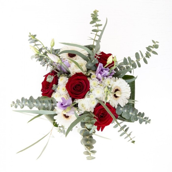 As a seasoned Highgate florist, I see this arrangement as a study in balance-each element distinct, yet together evoking the unique spirit of our neighbourhood. The white gerberas, creamy and expansive, radiate around their deep brown centres, lending an effortless sense of brightness to the design. Robust red roses spiral proudly at their side, embodying enduring love and classic style, much like the architecture flanking Highgate Village green. Lisianthus in lilac tones, appearing as scattered buds and blooms, bring a playful freshness reminiscent of the wildflowers seen beside Waterlow Park's ponds. Wisps of eucalyptus stretch upward, casting subtle shadows and infusing the bouquet with a crisp, invigorating scent. Further volume is created by the inclusion of soft, white filler flowers, their fluffy petals enhancing the overall sense of fullness and airiness. Dark, glossy leaves encircle the base, providing a sleek, polished finish, while the clear vase exposes the vibrant, freshly trimmed stems nestled in clean water-a testament to quality and longevity. Whether intended for a milestone birthday, a gesture of support, or to adorn a window overlooking Pond Square, this bouquet, crafted by Flowers Highgate, reflects the artistry and trust embedded in every floral creation we deliver to the heart of North London.