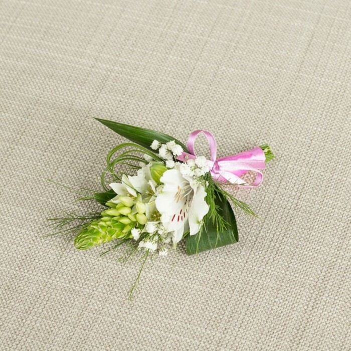 A beautifully composed boutonniere or petite corsage is laid out on a softly textured, light beige background that resembles natural linen, creating a calm, understated stage for the flowers to shine. Central to the piece is a white alstroemeria, its petals wide and slightly ruffled, revealing delicate reddish-brown speckles and fine veins that draw the eye inward to the flower's pale green throat and gently protruding stamens. Just to one side of this focal bloom, a dense, conical spike of bright lime-green buds forms a striking vertical accent; the buds are closely layered, giving the appearance of a sculpted, botanical tower that brings a contemporary edge to the otherwise classic design. Interlaced among the main elements are soft tufts of white baby's breath, each stem branching into tiny round blossoms that sit like floating dots of light, softening any hard lines and adding an almost ethereal haze. The arrangement is anchored by deep green, sword-like leaves and slim, grass-like strands that arc and weave outwards, introducing flowing lines and gentle movement reminiscent of a breeze over the lawns in nearby Highgate Wood. A slim, satin ribbon in a clear, bright pink is tied into a precise bow at the right side, its tails short and neat, the sheen catching the light to introduce a joyful, celebratory note. The lighting is even and natural, without harsh shadows, so every petal edge, leaf vein, and bud texture is clearly defined. This intimate floral piece, ideal as a groom's buttonhole, prom accessory, or special-occasion corsage, feels perfectly at home in Highgate-whether pinned on for a ceremony near Waterlow Park or worn to an elegant gathering along Highgate High Street-combining modern freshness with timeless romantic charm.