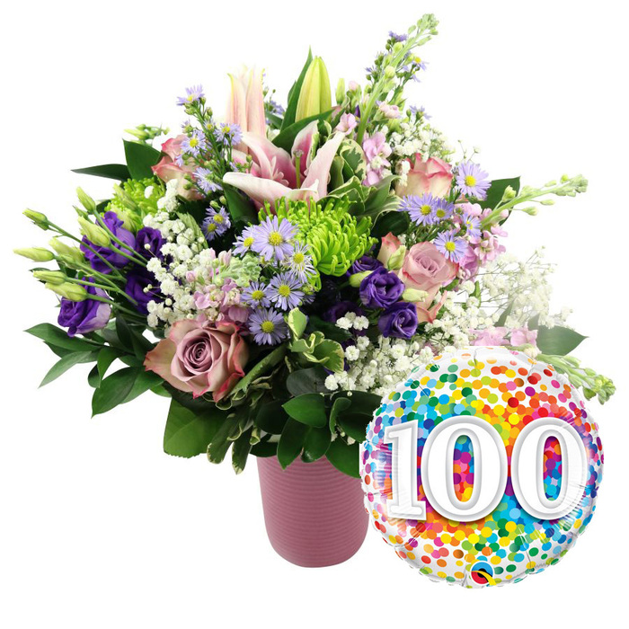 A joyful centenary scene unfolds against a bright white background, where a generous floral bouquet in a ribbed, dusty-pink vase is perfectly paired with a round foil balloon stamped with the number 100. The flowers have been arranged with the kind of layered detail and balance a local Highgate florist would bring to a truly special commission. Rising through the centre, large light pink lilies draw the eye, some fully open with wide, star-shaped petals and long stamens, others still poised as tightly held buds, suggesting time, growth, and the years yet to be cherished. Around them, soft pink roses and deeper mauve, almost dusty-rose blooms cluster closely, their velvety petals spiralling outwards and overlapping in intricate folds, evoking tenderness and affection that has built over a century. Slender stems of purple lisianthus weave between the roses, their ruffled blooms offering cool, satin-like accents, while sprays of small lavender asters with golden-yellow centres bring playful bursts of colour, reminiscent of the informal beauty found in gardens scattered around Highgate Village. Nestled throughout the bouquet, bright lime green button chrysanthemums provide contemporary, rounded accents, their tightly packed petals creating small, cushion-like forms. Airy white baby's breath drifts across the arrangement, softening edges and filling spaces with delicate clusters that look like tiny floating blossoms. A base of rich, dark green foliage supports the design, adding structure and the impression of freshly gathered greenery ready for delivery to a family gathering in Highgate or nearby Crouch End. Positioned to the lower right of the bouquet, a shiny foil balloon catches the light, its surface covered entirely in multicoloured confetti dots in vivid shades of red, orange, yellow, green, blue, and purple. At its centre, bold white numerals 100 appear slightly raised, clearly announcing a 100th birthday or centenary anniversary. The overall mood is one of warmth, honour, and joyous reflection, celebrating a full century of memories, love, and shared stories.