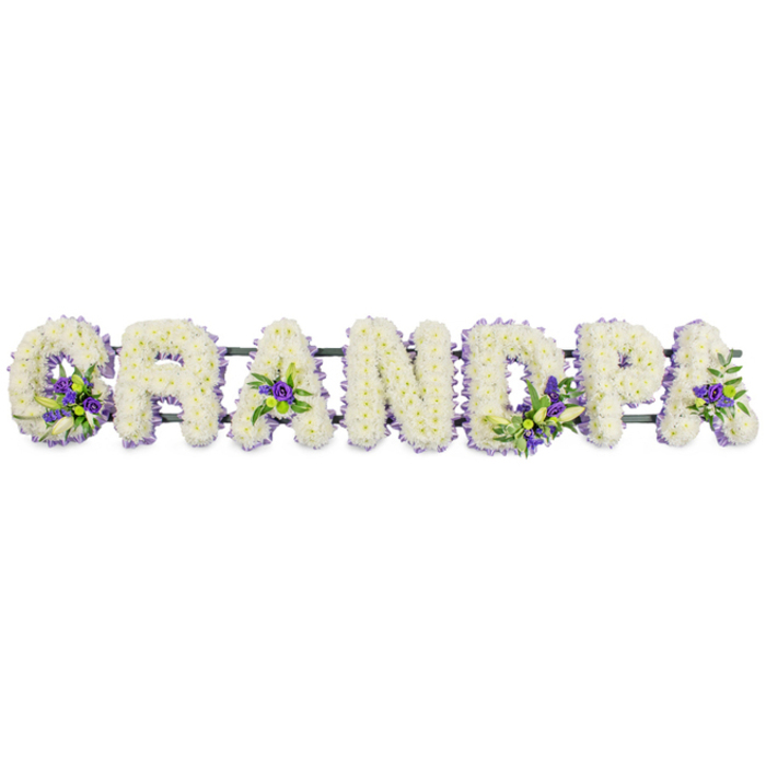 A poignant funeral flower arrangement forms the word GRANDPA in strong, block-style letters, aligned horizontally and photographed against a bright, uncluttered white background. Each letter is fashioned on a hidden frame and then completely blanketed with an abundance of small, white flowers, likely chrysanthemums or carnations renowned for their longevity and delicate texture. The petals are packed so closely that they create a continuous layer, shaping the letters into soft, rounded forms that look almost like white cushions. Interwoven within this sea of white are modest yet striking clusters of deep purple and lavender blooms, supported by fresh green foliage. These accent sprays are carefully spaced: one graces the sweep of the 'G', another settles in the centre of the first 'A', others rest within the 'D', on the curve of the 'P', and near the final 'A'. They bring gentle contrast and depth, suggesting quiet moments of reflection amid a pure, steady love. A dark green structural bar sits discreetly beneath all the letters, joining them into one coherent tribute that can be placed along a hearse, beside a casket in a Highgate chapel, or at a graveside where family members gather after the service. The colour palette of classic white with composed purple hints conveys reverence and remembrance, echoing the calm of nearby Highgate Woods or the contemplative paths of Highgate Cemetery. This kind of personalised GRANDPA tribute is often chosen when families want to speak directly to their loved one with flowers, using simple, heartfelt wording paired with careful, professional floristry.