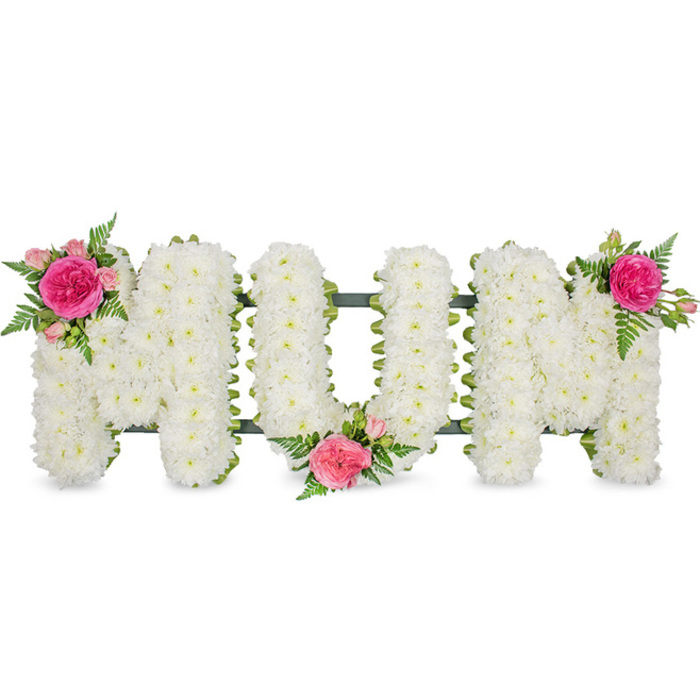 The floral arrangement in the image forms the word MOM in bold capital letters, each character clearly defined and aligned on a single horizontal plane. All three letters are completely filled with small white blooms-most likely spray chrysanthemums-placed so closely together that they create an uninterrupted field of white. The blossoms, with their layered, slightly curled petals, give the surface of each letter a plush, cushion-like texture, suggesting softness and serenity. A narrow strip of dark green frame or ribbon runs along the base, just visible beneath the mass of flowers, offering a quiet contrast and a sense of structural support. The simplicity of the white background and the even, diffused lighting keep the focus firmly on the floral craftsmanship. To introduce colour and emotion, three carefully balanced clusters of pink roses and greenery are woven into the design. At the upper left section of the first 'M', a fully opened fuchsia-pink rose is surrounded by paler pink spray roses, some only partly opened, and sprigs of fresh green leaves or fern. A similar cluster rests in the lower area where the 'O' and second 'M' meet, partially bridging the two letters. A final grouping crowns the upper right corner of the last 'M', echoing the first and creating a gentle visual rhythm across the tribute. The interplay of crisp white blooms with the rich pink roses and cooling greenery carries a quiet dignity, making this a heartfelt memorial piece for a mother. It feels perfectly suited to a Highgate setting, perhaps arranged by a local florist for a service near Highgate Cemetery or a chapel overlooking the leafy streets and rooftops, where families gather to say their goodbyes.
