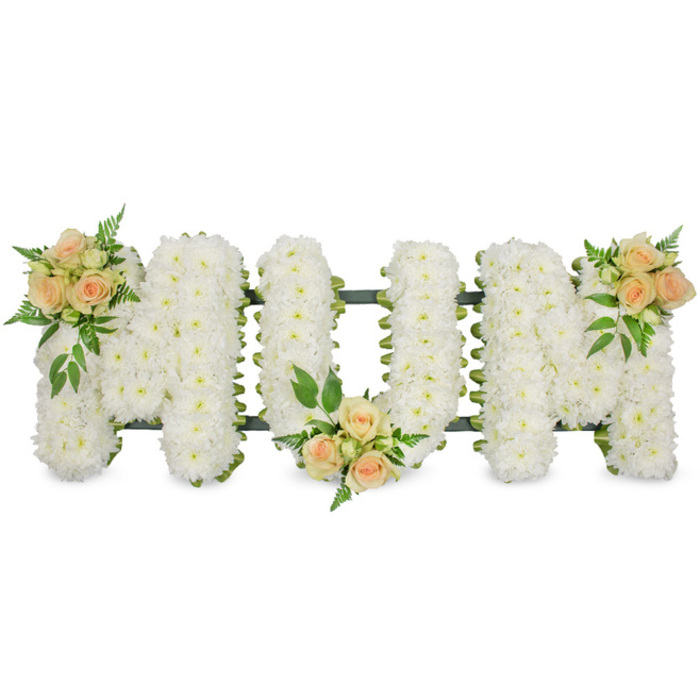 This photograph captures a tastefully designed MOM funeral tribute laid horizontally against a bright, seamless white backdrop, allowing every detail of the arrangement to stand out. The three block letters are entirely covered with pure white spray chrysanthemums, painstakingly arranged so that no greenery or mechanics show through the dense, cushiony layer of blossoms. The chrysanthemums' small, rounded blooms create a consistent texture from edge to edge, making the letters look pillowy and soft, embodying peace and remembrance. Just beyond the sea of white petals, a narrow outline of dark green ribbon or foliage follows the contours of each letter, enhancing legibility while adding a fresh, natural border. Bringing warmth and subtle colour to the piece, three clusters of peach and apricot spray roses are positioned along the tribute. The first cluster accents the upper left of the opening M, the second rests delicately at the bottom centre of the O, and the third sits at the upper right of the closing M. Each grouping contains roses at different stages-from tight buds to open blooms-surrounded by feathery fern fronds and small, glossy green leaves that spill lightly over the white chrysanthemum base. This careful interplay of white and soft peach tones expresses both purity and affection, making it ideal for farewell ceremonies around Highgate, where families often seek floral tributes that feel both elegant and heartfelt. The arrangement seems designed for display beside the coffin, perhaps in a quiet chapel or at a graveside service, its calm presence offering comfort and a visual reminder of a mother's enduring love and gentle guidance.