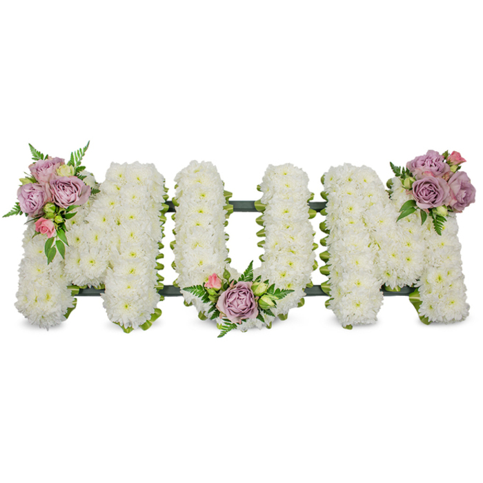 A large, dignified memorial piece spells out MUM in capital letters, each letter built up from hundreds of compact, pure-white chrysanthemums to form a plush, cloud-like surface that reads as both immaculate and comforting. The floristry is precise-blooms are densely set so the surface appears seamless, while a darker green framework, possibly ribbon-wrapped or moss-covered, traces the base and gives the letters a disciplined silhouette visible at the edges and between blooms. To soften the composition and add a personal touch, three clusters of soft lavender roses and pale pink buds are placed with considered balance: one embellishes the upper left arm of the first M, a second nestles into the inner curve of the U, and a third crowns the upper right arm of the final M. Each cluster includes glossy green leaves and ferny fronds that lift the pastel tones and introduce delicate movement across the white field. The result is both elegant and restrained-a sympathy tribute that reads as an emblem of love and remembrance. In the cool, diffused light often found in Highgate chapels or near the colonnades of Highgate Cemetery, the white chrysanthemums hold a serene, almost luminous quality while the lavender roses add a soft, consoling accent. Crafted with respectful attention and floral expertise by Flowers Highgate, this arrangement conveys deep affection and peaceful farewell, appropriate for a funeral service, wake, or graveside dedication for a mother or maternal figure in the local area.