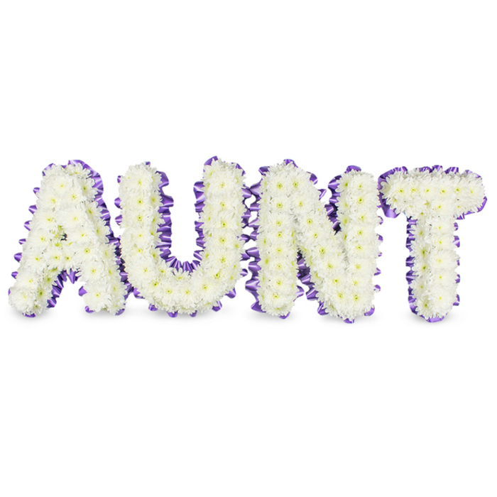 A carefully composed floral tribute spells the name AUNT in bold capital letters, each letter filled edge-to-edge with neat clusters of white spray chrysanthemums. The dense packing of small, ruffled petals produces a textured, almost cloudlike surface, while the occasional pale-yellow disc of each floret adds a soft, natural warmth to the overall white canvas. Around every letter, a deep purple satin ribbon is expertly applied - pleated and slightly ruffled to create a scalloped outline that provides a refined contrast to the purity of the chrysanthemums. Soft studio light falls evenly across the piece, producing delicate grey shadows beneath each character and emphasising the three-dimensional frames that hold the flowers. The smell is understated: a clean, green freshness more than perfume, suggestive of recently cut stems and the quiet of a florist's workbench. As a local craft offering from Flowers Highgate, this arrangement reflects the respectful tone often requested by families arranging services at Highgate Cemetery or small memorial gatherings in the village; its palette reads as both dignified and gently consoling. The construction shows careful attention to proportion and finish - the ribbon tucked, the flowers clipped to a steady profile - producing a tribute that communicates love and regard plainly and beautifully. It's a piece that serves as both a readable message and a tactile comfort in moments of farewell.