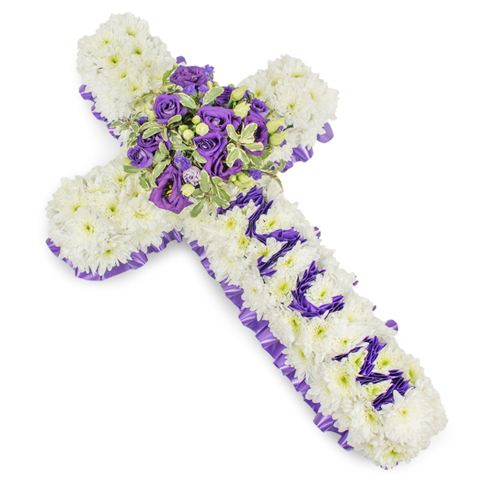 An elegant, substantial cross crafted for mourning, presented on a pristine white background to emphasise its textures and colours: the foundation is a dense carpet of pure white chrysanthemums, each bloom tightly nestled to form a seamless, cushion-like field that suggests purity and tranquillity. A narrow, ruffled purple satin ribbon traces the entire outer edge, its deep hue and soft sheen providing a solemn frame. On the central stem the letters MUM are formed in clearly defined purple flower clusters-probably eustoma or smaller spray chrysanthemums-standing out with thoughtful prominence against the white base. At the intersection of the arms a luxuriant central spray blooms: dark violet roses with tight, velvety petals sit alongside softer lavender lisianthus or eustoma, all layered with variegated foliage whose pale margins and richer centres add sculptural depth. Scattered green berries and fine leafy sprigs-reminiscent of pittosporum or eucalyptus-create subtle contrast and a natural, garden-like texture. The arrangement's cool palette, from whispered lavender to deep violet balanced by immaculate white, carries a mood of solemn dignity and tender remembrance. There's a delicate, powdery scent as if flowers were gathered after a light shower. Crafted in our Highgate workshop with attention to how it will be viewed in chapels and at gravesides-whether for a service near Pond Square, Waterlow Park, or Highgate Cemetery-this tribute from Flowers Highgate is composed to convey respectful farewell and enduring affection without florid display, offering comfort through simplicity, proportion, and heartfelt detail.