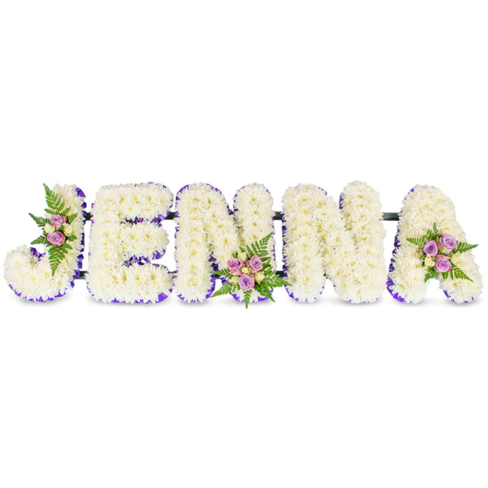 A tender, expertly made floral name tribute reads clearly as JENNA, each letter rendered in bold, three-dimensional form against a pristine white background. The letters are densely composed from hundreds of small, creamy white chrysanthemums or similarly delicate petals, producing a soft, clouded surface that invites a gentle, contemplative gaze. A vivid yet restrained purple trim - either ribbon or tiny matching flowers - traces the base and inner contours of each character, creating a crisp silhouette that lifts the white blooms from the backdrop. Carefully placed on three letters are small, artful clusters of blush pink and lavender spray roses, accented by lighter cream or pale yellow rosebuds and fresh fern fronds; these are set on the J, the lower centre of the first N, and the upper curve of the A, bringing discreet colour and organic texture to the overall design. Slim dark bars run horizontally, linking the letters and revealing the solid frame beneath without distracting from the florals. The composition is lit softly, the petals catching a cool daylight that suggests morning services near Highgate's churches or a farewell laid by the gates of Highgate Cemetery. As a florist familiar with local tastes around Archway Road and the Village, I see this arrangement as a composed, personalised expression of remembrance - serene, respectful, and made to be read easily from a distance while offering close, comforting detail to those who lean in.