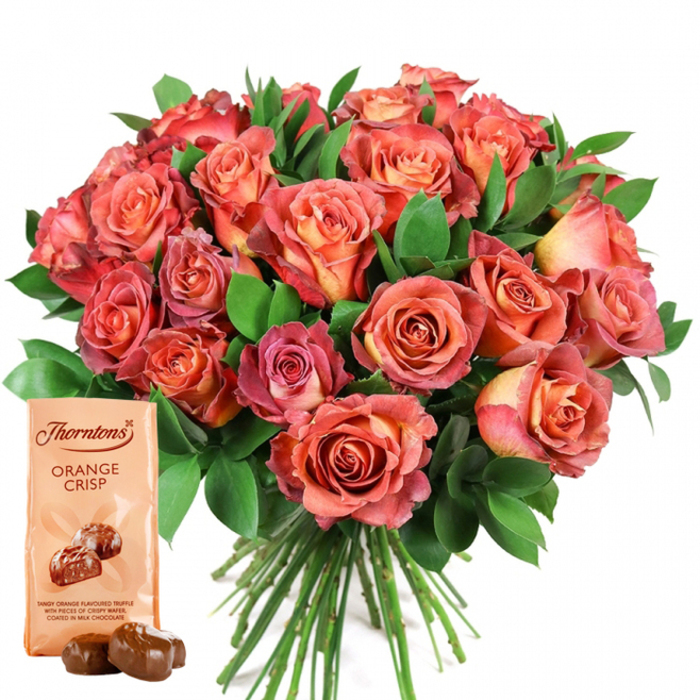 Dominating this luminous scene is a lush, hand-tied bouquet of roses, masterfully assembled and radiating warmth against an understated white background. The roses, central in the composition, boast a gradient of hues that begins with rich apricot and peachy-orange at the heart of each flower and deepens through to saturated coral, rosy pink, and reddish-pink at the tips of their gently unfurling petals. Their velvety surfaces create an impression of sumptuousness and classic romance, while abundant greenery-likely eucalyptus and glossy ruscus-fills the spaces between, amplifying the vibrancy and fullness of the bouquet. Neatly gathered stems visible at the base hint at the skilled work of a florist dedicated to Highgate's unique blend of elegance and tradition. In the lower-left, a Thorntons Orange Crisp chocolates pouch stands out in delicate beige, displaying the renowned branding and a detailed image of two inviting orange-infused truffles. The lower script describes the decadent content: tangy orange truffle with layers of crispy wafer, all covered in creamy milk chocolate. As a finishing touch, two real chocolate truffles are arranged in front, their surfaces glossy and rounded. This evocative pairing of exquisite roses and gourmet chocolate is the perfect gift for marking milestones-Mother's Day, birthdays, or anniversaries-delivered with care by local Highgate florists, celebrating both artistry and heartfelt generosity.