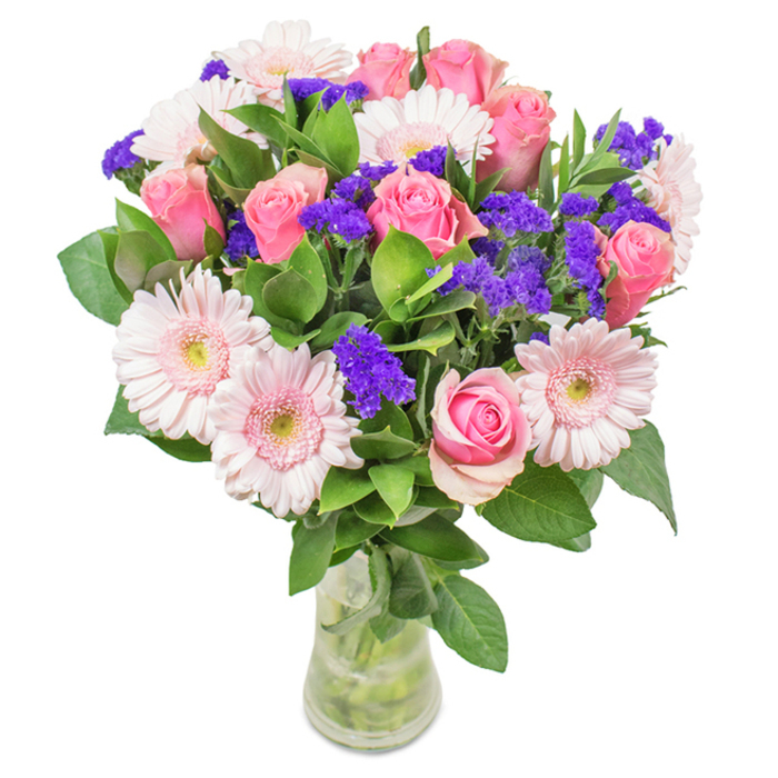A striking, hand-arranged bouquet presented in a crystal-clear glass vase, photographed against a pure white background-a familiar scene in Highgate's renowned florists' shops. The dominant element is a grouping of seven to nine medium pink roses, their petals at varying stages: some tightly rolled and others partially opened in signature spiral formation, evoking understated romance. These are beautifully contrasted by five to seven light pink Gerbera daisies, their generous round heads and pale, almost white centers catching the subtle natural light. Throughout, clusters of vivid purple statice are artfully distributed, offering a dramatic pop of colour and refined textural dimension. Anchoring the composition is an abundance of deep green foliage, evoking the mature trees lining Highgate's historic streetscapes, bringing freshness and visual balance. Transparent water in the vase complements the healthy, carefully cut stems, suggesting a recent delivery or thoughtful gift. Ideal for occasions such as birthdays, anniversaries, or simply as a stylish centrepiece for a Highgate home or workspace, this arrangement radiates joy and affection-each flower selected for beauty and meaning, and arranged with professional care.