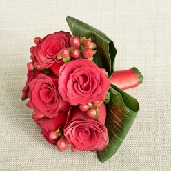 On a softly textured, light beige fabric that could easily be a linen table runner in a Highgate Village home, a hand-tied bouquet of deep red roses lies in quiet focus, captured from a slightly elevated angle. The roses are lush and full, each blossom composed of velvety petals that spiral from a tightly furled centre into gently opening outer layers, shifting in tone from near-burgundy at their depths to a brighter crimson on the edges. Between these romantic blooms nestle neat clusters of small, rounded Hypericum-like berries in shades of reddish-pink and warm red, their polished, bead-like surfaces offering a youthful counterpoint to the softness of the petals. Wrapping the arrangement, broad, dark green leaves curve around the flowers in smooth, architectural sweeps, their subtle veins and glossy texture giving the design a contemporary, almost sculptural feel. At the base, a rich red satin ribbon secures the stems in a snug band, its slight sheen catching the light and tying the colour story together. The lighting is gentle and even, reminiscent of a calm afternoon by Waterlow Park, accentuating the interplay of textures-the plush roses, firm berries, and sleek foliage. This bouquet feels designed for a bridesmaid walking through a Highgate wedding venue, a romantic anniversary dinner on Swain's Lane, or a thoughtful thank-you gift, carrying a mood of sophisticated passion and understated luxury that speaks of expert, local floral artistry.
