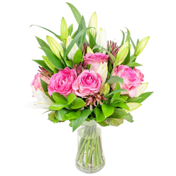 Presented in a plain clear glass vase set against a bright white studio background, this bouquet carries the quiet confidence of a Highgate floral design crafted for everyday moments and special occasions. Dominating the arrangement are a cluster of large, fully bloomed deep pink roses whose velvety petals fold in rich layers of fuchsia and blush, each bloom offering a soft, familiar perfume. Slender white lily buds rise through the roses, a mix of tightly closed, elongated forms and those beginning to open into trumpet-shaped petals with delicate green hints at their bases. The composition is built on abundant green foliage - broad, glossy leaves and finer, lighter-green sprigs - which together provide volume and a lively, fresh backdrop that accentuates the roses and lilies. Subtle darker burgundy and reddish-brown accent buds are tucked into the greenery, giving the bouquet depth and a textured, seasonal note. The vase reveals trimmed stems immersed in clear water, the slightly tapered base lending understated elegance and stability. In my experience delivering to addresses around Swains Lane and the lanes near Highgate Cemetery, neighbours often choose arrangements like this to mark anniversaries, thank-you gestures, or to brighten a Hampstead Heath-facing window. The lighting in the photo is clean and natural, emphasizing petal texture and glossy leaves, and the overall effect is one of thoughtful, hand-crafted freshness - a floral statement that balances romance with restraint. Flowers Highgate would describe this as a go-to bouquet for local gifting when a thoughtful, beautifully balanced arrangement is needed.