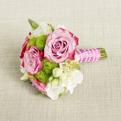 A compact hand-tied bouquet rests serenely on a neutral, light beige fabric, its fine, natural texture reminiscent of linen napkins set for a Highgate village brunch. The flowers lie horizontally, inviting the eye to travel from the neatly wrapped stems on the right across to the open faces of the blooms on the left. Three pink roses form the emotional centre of the posy, two larger and one slightly smaller, their petals unfolding in generous spirals. The colour shifts from a soft, powdery blush in the inner petals to a deeper, almost magenta pink along the outer edges, where the ruffled contours create depth and gentle drama. Between the roses, clusters of lime-green button chrysanthemums offer a lively counterpoint. Each spherical head is densely packed with tiny petals, giving a cushioned, almost moss-like texture that feels youthful and modern against the more traditional roses. Threaded through the design are creamy white blossoms, probably lisianthus or freesia, adding a veil of lightness and soft, fluttering shapes. Tiny, star-like white flowers with golden centres, suggestive of waxflower or stephanotis, punctuate the arrangement and lend a bridal delicacy. The stems are bound tightly by a vivid fuchsia satin ribbon, smooth and glossy, which forms a comfortable handle for carrying along Highgate's leafy streets to a ceremony at a local church or registry office. Over the ribbon, a single strand of petite white faux pearls wraps diagonally, catching the light with each curve and giving the bouquet a refined, almost vintage charm. The lighting in the image is even and gentle, with no sharp shadow, allowing every petal edge and textural nuance to show clearly and underscoring the bouquet's suitability as a bridesmaid's posy or intimate bridal bouquet for a small city wedding or engagement celebration.