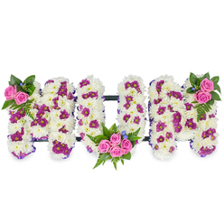 This heartfelt tribute forms the word MUM in bold, three-dimensional letters, each letter fashioned from a dense mass of pristine white chrysanthemums that give the piece a plush, pillow-like surface. Scattered through the white base are deliberate touches of deep magenta and purple spray chrysanthemums which create soft patterns and depth without overpowering the purity of the white. Three clusters of lively pink spray roses punctuate the composition: a modest cluster at the upper left of the first M, a fuller bouquet of four or five pink roses tucked into the lower curve of the U with surrounding fern fronds, and a balanced mirrored cluster at the upper right of the last M. Dark green foliage - ferns and mixed leaves - provides a rich, shadowed backdrop while small blue accent flowers glint like tiny beads among the greenery.

A narrow, dark horizontal bar links the letters, lending a discreet frame and stability to the arrangement, and a delicate purple ribbon traces the outer edges on some designs, subtly defining the letterforms. Bathed in soft morning light this tribute reads as tender and composed; the chrysanthemums' texture is almost audible in its density, and the pink roses offer a warm, reassuring focal scent. The overall palette - white, magenta, pink and blue - balances solemnity with gentle affection.

Prepared with the local knowledge of Highgate floristry and attention to bespoke sympathy work, this piece is appropriate for services at Highgate Cemetery, a family wake in Highgate Village, or quiet remembrance gatherings near Pond Square. Flowers Highgate prepares and handles such tributes with the sort of careful craft and local delivery sensibilities neighbours expect.