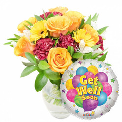This photograph presents a cheerful "Get Well Soon" arrangement that feels both reassuring and bright, composed with the care of a local florist. Dominating the left side is a lush bouquet of warm orange and deep yellow roses whose velvety petals spiral open, paired with vivid yellow gerbera daisies whose flat, sunny faces project optimism. Textural contrast comes from rich maroon carnations, their ruffled edges adding depth, while fine clusters of white alstroemeria peek through to soften the palette and introduce a delicate scent in the mind's eye. Verdant greenery cradles each bloom, creating a natural, layered silhouette, and the clear glass vase reveals the stems and water, suggesting freshness and straightforward craftsmanship. At the lower right, a glossy round Mylar balloon partially overlaps the blooms; its silvery field reflects light and provides a playful frame for a colorful cluster of illustrated balloons in blue, purple, green, pink and yellow, decorated with stripes, dots and small checker patterns. Bright yellow-and-blue lettering in the centre reads "Get Well Soon," outlined with a faint shadow to make the message pop, and tiny starbursts dance along the balloon's border. A modest "KALEIDOSCOPE" logo appears at the edge. As someone who arranges flowers for neighbours across Highgate and near Hampstead Heath, I see this as an ideal recovery gift: visually uplifting, tender in scent and texture, and ready for same-day delivery to a bedside or front door to remind a loved one they are cared for.