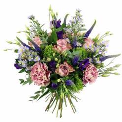 Set against a bright white background, this rounded bouquet appears full to bursting with layers of blush, mauve, and purple blooms, all resting on a bed of lively green foliage. The first flowers you notice are the roses, their petals a soft pastel pink with some blossoms edged in a slightly deeper blush, creating a subtle gradient from centre to tip. Some roses remain gently cupped, while others are more open, revealing the familiar, romantic spiral at their heart. Cradling these are lush carnations in dusty rose and soft mauve tones, each one rich with frills that give a delightful, tactile depth to the design. Punctuating the arrangement, slim spires of deep indigo-violet Veronica rise up and out, their elongated form and textured surface bringing height and a painterly sense of movement. Between the larger blooms, rich purple lisianthus flowers cluster in velvety cups, supported by buds that promise more blossoms to come. Fine sprays of tiny, star-shaped aster-like flowers in lavender-blue scatter throughout the bouquet, adding a light, daisy-like touch that softens the overall effect. The blooms sit within a collar of varied greenery: bright lime-green filler, possibly bupleurum or a similar textural foliage, offers a lively contrast, while cooler, sage-green eucalyptus leaves arc gracefully, adding both structure and a gentle aromatic note. At the base, neat green stems are bunched and tied, confirming this as a hand-tied bouquet designed to slip easily into a vase in a Highgate home, perhaps overlooking the trees near Hampstead Lane or Queens Wood. The overall mood is elegant yet approachable, making it perfect for marking a thoughtful moment such as a birthday, a quiet anniversary, or a simple gesture of appreciation delivered across N6.