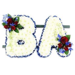 This bespoke funeral tribute presents the initials "BA" as two freestanding floral letters, each meticulously formed from a blanket of small, immaculate white chrysanthemums that create a cloud-like, textured surface. A ruffled royal blue satin ribbon traces the outer contours of both letters, providing a solemn, contrasting frame that reads as both respectful and refined. The 'B' bears a lush accent at its upper left: several deep red roses in varying stages of bloom, paired with intensely blue, delphinium-esque spikes and softened by darker green foliage and light green trailing tendrils. The 'A' carries a complementary cluster at its lower right, mirroring the red-and-blue palette and lending visual balance. The pair is secured on a low, dark green rectangular base, allowing the arrangement to stand together as a single tribute. In gentle, diffused light the white chrysanthemums take on a soft luminescence while the velvety roses give off a quiet, familiar scent-the kind you might notice in a calm corner of Highgate Village after a florist's early-morning delivery. As crafted by Flowers Highgate for families around Highgate, Highgate Wood and nearby Archway, this piece reads as an intimate, personalised message of remembrance - the colours and textures chosen to express peace, love and enduring respect without words.