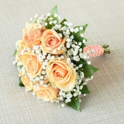 Embracing the tranquil elegance of Highgate, this softly luminous bouquet presents a classic harmony of seven to eight lush, peach-apricot roses, their petals alive with delicate gradations of colour. The blooms are skillfully interlaced with airy white sprays of baby's breath, each cluster reminiscent of gentle morning clouds floating above Highgate Wood. Rich, emerald leaves provide a subtle, grounding base, their refreshing greenery peeking out between the layered petals for natural balance. Securing the gathered stems, a plush, coral-peach satin ribbon spirals gracefully, accented with tiny, lustrous pearls that shimmer delicately-a detail echoing timeless bridal celebrations in Highgate's historic chapels. The bouquet sits upon a neutral, subtly woven backdrop like those found in the local artisan shops, focusing attention on the flowers' radiant palette. Even, dappled light illuminates every element, revealing velvety petal layers and glistening pearl accents. Each nuance-from the subtle blush of apricot roses to the cloud-soft flecks of gypsophila-creates an arrangement that radiates grace and emotional warmth. Perfect for a bride walking along Swain's Lane or for a cherished anniversary gift, this bouquet embodies Highgate's unique blend of heritage, peacefulness, and refined artistry.
