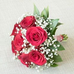 Poised delicately on an ivory-hued linen, a hand-tied bouquet radiates romance and grace, instantly conjuring images of celebrations along Highgate's leafy lanes. The focal point is a cluster of red roses in their prime-their velvety petals unfurl in lush spirals, each blossom a testament to enduring love and special moments shared. Surrounding the roses are clouds of fine, white Gypsophila, infusing the arrangement with a silken weightlessness reminiscent of gentle Highgate morning fog. Emerald-toned leaves emerge amid the flowers-perhaps ruscus or native evergreens-reflecting the abundance of lush parks and tree-lined avenues that define the local landscape. The stems are carefully wrapped with a vibrant red and white striped ribbon, elegantly finished with a winding thread of white pearls, a nod to both tradition and contemporary sensibility. The bouquet's textures-smooth petals, feathery baby's breath, and satin ribbon-invite the touch, and its balanced silhouette radiates skilled craftsmanship. Subtle, diffused light highlights each detail: the interplay of the rose's deep reds, the pearly white accents, and the surrounding fresh foliage. This bouquet, with its inviting fragrance and superb composition, would be at home at a Highgate wedding, as an anniversary surprise on Highgate Hill, or resting on a reception table at Lauderdale House. It offers not just flowers, but a sensory experience, an expression of joy and devotion shaped by the neighbourhood's creative florists.