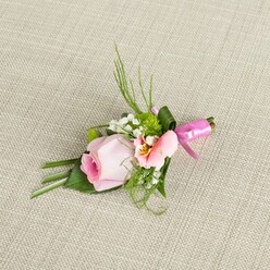 Bathed in gentle light, this Highgate-crafted boutonniere lies diagonally across a subtle, light beige woven background, as if waiting to be pinned before a celebration along Pond Square or at Lauderdale House. At its core, a meticulously coiled rose in blush pink emerges, its petals transitioning from a deep, cool pink heart to soft outer edges, promising freshness and gentle romance. A lighter flower, perhaps an Alstroemeria or lisianthus bloom in peach blush, sits alongside, displaying a flare of yellow near the centre amidst feathery dark markings that catch the eye. Cloud-like tufts of baby's breath are interspersed throughout the composition, their white softness mirrored by tiny, vibrant green cushion mums tucked amidst the greens. The foliage, both slender and broad, adds volume and depth-some blades arching upwards, others gracefully folded beneath the blooms. A wide, dark green leaf encircles the bound stems, which are secured with a vibrant, glossy fuchsia ribbon tied into a delicate bow whose sheen echoes festive Highgate gatherings. The tightly woven, lightly textured background acts as a simple yet refined stage, amplifying the freshness and colour of each element. This piece, meticulously composed by skilled Highgate florists, is ideal for weddings, formal events, or proms across North London-its elegant palette and lush greenery embodying the charm and quiet celebration characteristic of this community.