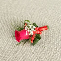 A handcrafted boutonniere is displayed on a pale beige, slightly nubby linen fabric, the subtle weave giving a natural, Highgate-townhouse feel to the scene. At its centre, a single fuchsia rose draws the eye, its petals rich and velvety, spiralling tightly at the core and relaxing into soft curves at the edges. The rose feels freshly cut, as if it has just been prepared in a local flower shop for a groom about to walk through the leafy streets near Highgate Village. Surrounding the bloom is a delicate halo of white baby's breath, the tiny star-shaped flowers creating a light, airy frame that softens the strong pink. Tucked among these are small scarlet-red hypericum berries, rounded and lustrous, adding warmth and a playful touch that hints at celebration and good cheer. Fine, feathery green foliage extends outward, giving movement and a slightly wild, botanical feel, while broader, darker leaves are carefully curled close to the stem, lending structure and polish. The stems are tightly bound in smooth red satin ribbon, finished with a neat bow that lies flat and comfortable against where a jacket would be. The lighting is gentle and even, accentuating the textures: the matte softness of petals, the sheen of berries, the silkiness of the ribbon, and the tactile fabric beneath. This small piece is photographed from above, capturing its balanced shape and thoughtful composition, ideal for weddings, proms, or formal evenings across Highgate and nearby Muswell Hill, where understated elegance and a touch of colour are all that's needed to mark a special moment.