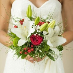 On a Highgate wedding morning, artistry and emotion blossom in this elegant hand-tied bouquet, lovingly gathered by a local expert. The scene finds a bride, her beautifully textured white gown framing a bouquet that resonates with the area's unique blend of tradition and creativity. Snowy oriental lilies open luxuriously, their petals unfolding to reveal golden stamens and releasing a gentle, sweet scent like a stroll through Waterlow Park in early June. Nestled within, rich crimson roses pulse with heartfelt passion-their colour grounding the bouquet just as the leafy avenues of North Road anchor the community. Clusters of joyful red berries and playful green button dianthus add refreshing pops and round forms, creating visual intrigue and natural movement. Gossamer sprays of gypsophila float between the central blooms, reminiscent of morning mist along Highgate Woods' edges, giving the whole composition a sense of lightness and grace. The arrangement is finished with feathery greenery and glossy broad leaves, each stem thoughtfully placed to celebrate devotion, hope, and natural beauty. This bouquet stands as a tribute to love's timeless journey, its colours and textures weaving into Highgate's vibrant local tapestry, prepared for marriage ceremonies with a sense of place and memory.