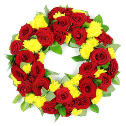 This image shows a refined circular wreath designed as a funeral or memorial tribute, set against a clean white background so that every detail of the flowers is clearly visible. The wreath is crafted primarily from deep red roses, each bloom carefully opened to reveal the classic spiral at its centre, giving the arrangement a feeling of romance and profound respect well suited to farewells in Highgate's historic churches or the grounds of Highgate Cemetery. The roses display a range of reds, from bright, heartfelt crimson to darker, wine-infused tones, creating natural highlights and shadows across the ring. Nestled between these larger blooms are generous groups of small yellow chrysanthemums, whose many fine, densely packed petals form soft, cushion-like heads. The yellow brings a gentle, uplifting note, like sunlight breaking through trees in nearby Waterlow Park, softening the intensity of the red and suggesting comfort, remembrance, and gratitude. Around and underneath the flowers, fresh green foliage fills the spaces, likely a mix of salal and eucalyptus with varied textures: some leaves appear plump and glossy, others more slender and muted with a dusty, silvery-green finish. This greenery frames the blossoms without overwhelming them, adding depth and a natural rhythm to the design. The wreath is flawlessly circular, with an open centre that invites thoughts of eternity, continuity, and enduring love. The bright, even lighting ensures each petal and leaf is sharply defined, and the simple white backdrop keeps attention firmly on the floral tribute, making it a quietly powerful choice for commemorations, funerals, or remembrance services across the Highgate area.