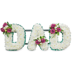 A solemn yet tender memorial piece, this three-dimensional display spells DAD in large, sculpted capitals composed entirely of pristine white chrysanthemums, their round, petalled faces packed closely to create a seamless, clouded surface. Each letter is sharply outlined with an emerald-green ruffled ribbon, the vivid trim lending a formal, almost architectural clarity against the snowy blooms. Behind the letters a discreet dark green or grey horizontal rail gives the arrangement structure and the sense of a stable, self-supporting tribute prepared for a funeral or graveside service. At key points on each letter sit small clusters of rich magenta roses, some in bud and some gently opening, accompanied by tiny white freesia-style blooms and glossy dark foliage to anchor the colour. The first D carries its bouquet on the upper left curve, the A's cluster nestles in the lower central V, and the final D echoes this with a cluster on the upper right curve - a deliberate, comforting symmetry that reads as affection in floral form. The mix of textures - soft chrysanthemum heads, velvet rose petals, crisp ribbon edge - is accentuated by soft studio light against a plain white backdrop, giving the tribute both presence and delicacy. As a local florist familiar with Highgate Village, Waterlow Park and the surrounding neighbourhoods, I would suggest this design for a family who wants a classic, personalised farewell: dignified, tactile, and quietly expressive of love and remembrance, available for careful delivery across Highgate and neighbouring Hampstead.