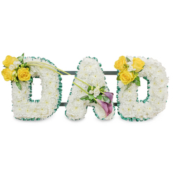A dignified and personal memorial piece shapes the word "DAD" in three dimensional capital letters, each letter formed from a compact, even carpet of immaculate white spray chrysanthemums that read as soft, textured surfaces under soft studio lighting. The perimeter of each letter is neatly finished with a ruffled, dark green satin ribbon that provides a strong, botanical frame and elegant contrast to the white flowers. Narrow, dark support bars are visible running behind and between the letters, a discreet structural detail that keeps the trio united as a single, balanced tribute. The left 'D' is punctuated on its upper left curve by a bright cluster of 3-4 yellow roses-sunny and open-paired with delicate white freesia-like fillers and glossy green foliage; two elongated, bare green stems extend upward and diagonally toward the centre, adding a sense of movement and connection. On the lower left diagonal of the central 'A' sits a refined grouping anchored by two deep purple calla lilies, their sculptural, trumpet shapes introducing a solemn, elegant note, complemented by tiny white accents and slender greenery. The right 'D' mirrors the left with the same cheerful yellow rose cluster on its upper right curve, creating a symmetrical rhythm across the display. Set against a plain white background, the arrangement reads as both contemporary and respectful-white for peace, yellow for affectionate remembrance, and purple for reverence-making it an appropriate floral choice for a funeral or memorial service in Highgate, whether being sent from a nearby chapel on Swain's Lane or arranged for a family gathering near the Pond.