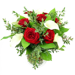 An opulent arrangement of red roses and white calla lilies is displayed in a clear glass vase, photographed against a clean white background that allows the colours and textures to shine with clarity. At the heart of the bouquet, a cluster of around six or seven roses unfurls fully, each bloom saturated in a deep crimson hue, velvety petals curling into tight spirals that speak of enduring love and heartfelt emotion. Interlaced between them, several graceful calla lilies in pure white introduce a sculptural calm; their smooth, trumpet-like petals rise and curve gently, revealing slender yellow spadices that glow softly at the centre of each bloom. Surrounding these focal flowers, a rich collection of greenery adds depth, movement, and natural charm: rounded eucalyptus leaves in cool, silvery-green tones give the arrangement a soft, airy character, while larger, darker green leaves provide a solid, lush frame. Through the cylindrical vase, you can see the tidy bundle of stems immersed in clear water, and a subtle ribbed band at the vase's base catches the light with understated detail. The bright, even lighting used in the photograph enhances the contrast between vivid red, crisp white, and layered greens, suggesting the freshness of flowers just prepared for delivery across Highgate, from the leafy paths near Hampstead Heath to the quiet terraces off North Road. The mood of the bouquet is both romantic and composed, making it an ideal choice for marking an anniversary, celebrating an engagement, or bringing an elegant touch to a dinner party in one of Highgate's period homes, where style and sentiment go hand in hand.