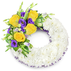 A pristine funeral wreath shaped as a perfect circle, photographed on a plain white background, designed to speak of sympathy and peaceful remembrance. The majority of the ring is formed from tightly clustered white spray chrysanthemums; their many small petals overlap to create a pillowy, uniform surface-soft in appearance, symbolically pure, and giving the wreath a comforting, cloud-like texture. Nestled on the upper left quadrant is a vibrant spray of colour: rich yellow roses in full bloom, their petals unfurling in warm, buttery spirals, paired with luxurious, deep purple Eustoma (lisianthus) whose satiny, ruffled cups lend a velvety coolness to the arrangement. Several unopened lavender-toned lisianthus buds and tiny green shoots add natural variation and a sense of quiet progression. Variegated and glossy foliage, along with delicate ferny fronds, threads through the cluster to balance the composition and accentuate the blooms' hues. A discreet dark purple mesh ribbon traces the wreath's inner and outer edges beneath the chrysanthemums, a subtle detail that ties the design together and echoes the purple blooms. Freshly assembled and mindful of local traditions, this piece reflects the kind of respectful tribute often ordered for services at Highgate Cemetery or delivered to family homes around Highgate Village. Flowers Highgate prepares wreaths like this with careful craftsmanship and attention to texture and scent, offering a gentle, dignified expression of condolence for those in the neighbourhood.