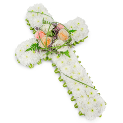 This image captures a refined Christian cross crafted entirely from fresh flowers, displayed against a simple white backdrop that allows its thoughtful details to come forward. The main body of the cross is densely carpeted with small, pristine white chrysanthemum heads or similar blossoms, placed close together to form a continuous, cloud-like texture. The white blooms convey purity, innocence, and a gentle sense of spiritual comfort, as though the cross itself were softly illuminated from within. Tracing the perimeter is a narrow edge of bright green foliage, perhaps compact leaves or button chrysanthemums, that crisply outlines the arms and vertical stem. This green edging evokes the calm, natural beauty found in and around Highgate, from the tree-covered paths of the cemetery to the green pockets tucked behind historic houses. At the intersection of the cross's arms, a central floral spray adds warmth and focus. Several roses in soothing pastel hues-soft peach, pale blush, and creamy white-open fully, their velvety petals layered in elegant spirals that seem to hold cherished memories. Around them, delicate fern fronds, slim arcs of grass, and a scattering of small purple filler flowers create gentle movement and depth. The arrangement is lit with even, diffused light, highlighting the contrast between the velvety roses and the cushiony chrysanthemums without any harshness. This sympathy cross would be fitting for a funeral or remembrance gathering in Highgate, expressing condolences and faith in a quiet, dignified way. It offers a comforting visual presence at the front of a chapel, by a graveside, or in a memorial space, honouring a life with beauty and grace.