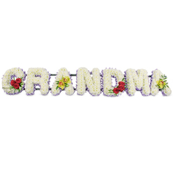 The image presents a heartfelt floral tribute spelling GRANDMA in large, carefully crafted block letters, set against a crisp white background that allows every flower to be clearly defined, as if it had just been arranged in a peaceful Highgate funeral home. Each letter is densely filled with white chrysanthemums or similar compact blossoms, their tightly clustered petals overlapping to create a plush, uniform surface that looks invitingly soft, like a cushion of petals. Along the lower edge of each letter runs a gentle border of pale lavender or light purple flowers, a subtle accent that frames the shapes without distracting from the calm, snowy white, much like the muted tones of stone and foliage along Swain's Lane. The G is adorned at its lower left curve with three deep red roses, their rich colour and glossy green leaves forming a vivid statement of love and remembrance. The first A features two yellow-green orchids with warm reddish-brown centres, positioned along its crossbar to introduce an elegant, contemporary note. The R, N, and D hold their form in pure white, edged with lavender, their simplicity conveying respect and tranquility. On the M, another cluster of three deep red roses nestles in the lower right section, echoing the sentiment of the G and drawing the eye through the middle of the design. The final A repeats the pairing of green orchids, closing the word with the same distinctive touch that begins it. Behind the flowers, a narrow dark metal frame supports the letters in a single line, almost invisible from the front. This GRANDMA flower tribute is a classic, personalised choice for funerals and memorials in Highgate, offering a dignified and loving farewell to a much-loved grandmother.