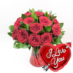 In this image, a lavish bouquet of deep red roses is presented with the polished elegance you'd expect from a skilled Highgate florist. Around a dozen or more roses are massed together into a generous, rounded cluster, each flower rich with layers of velvety petals. Some blooms are fully open, their centres revealing intricate spirals that seem to draw the eye inward, while others remain partially furled, suggesting a romance still blossoming. Threaded among the flowers is a halo of vibrant green foliage, the leaves fresh, smooth, and slightly glossy, their cool tones creating a pleasing contrast with the warm, intense reds. The stems are gathered in a ruby-red glass vase, whose clear yet tinted sides feature gentle fluted ridges. Light glances off these vertical lines, giving the impression of delicate movement and fine craftsmanship. Just in front of the vase, positioned slightly to the lower right, a bright red heart-shaped foil balloon leans forward as if eager to share its message. The metallic surface shines and reflects light, reminiscent of festive decorations in the windows along Highgate High Street. Across the centre of the heart, the words "I Love You" appear in flowing white cursive script, unmistakable and sincere. A stylised silver arrow, reminiscent of Cupid, is shown piercing the heart from bottom left to top right, adding a timeless romantic symbol. All of this is set against a clean white background that strips away distraction, allowing the bold reds, lush greens, and shimmering metallics to stand out. The image conveys a clear sense of passionate affection, ideal for Valentine's Day, anniversaries, or any special moment when someone in Highgate wants to send an unmistakable declaration of love.