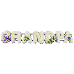 The image presents a serene and personalised floral tribute that spells out GRANDPA in large, upright letters arranged in a straight line, as you might see resting along the side of a coffin or on stands at the front of a chapel in Highgate. Each letter is completely filled with small, creamy white blossoms, resembling chrysanthemums or carnations, that have been placed so close together they create a smooth, velvety blanket of petals. The compact blooms soften the otherwise bold shapes, giving the word an inviting, almost gentle presence. Breaks in the white come from carefully positioned clusters of deep purple and lilac flowers, threaded with touches of fresh greenery. These touches of colour appear at the base of the 'G', inside the first and last 'A', and within the strokes of the 'D' and 'P', acting like small bouquets set into the letters themselves. Beneath the flowers, a green support bar quietly joins the individual frames, mostly hidden from sight but essential for holding the word secure and level. The composition feels composed and tranquil, suitable for a reflective service near Highgate Cemetery or a small family farewell in a local church off Swains Lane. The interplay of pure white and composed purple tones conveys respect, love, and a sense of calm, making this GRANDPA lettering a fitting choice when a family wishes to express how central their grandfather was to their lives. It captures the quiet craftsmanship of a florist used to guiding families through difficult goodbyes with care and attention to detail.