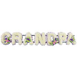 This image features an elegant memorial flower arrangement spelling out GRANDPA in seven sturdy block letters, displayed on a crisp white backdrop that highlights the colours and forms. Each letter is meticulously composed from a thick blanket of small, snowy white chrysanthemums or similar funeral blooms, creating a velvety, plush surface that suggests comfort and care. The outer edge of every letter is neatly trimmed with a fine border of small lavender and purple flowers-perhaps statice or dainty heather-which gently trace the contours and lend the tribute a soft, serene halo of colour. Within several of the letters sit carefully placed accent clusters: the 'G' and the first 'A' carry sprays of white, lily-like flowers, rising gracefully among pink and fuchsia blooms and touches of deeper purple, all anchored in dark green foliage. The central 'D' and the second 'A' echo this mix, and in some areas, tiny bright green button chrysanthemums provide a fresh spark of brightness. A slim, dark green frame bar runs behind the letters, nearly invisible yet essential for holding them evenly in place, as you might see on a stand at a funeral in Highgate Cemetery or a quiet service in nearby Kentish Town or Tufnell Park. The lighting is even and gentle, enhancing the freshness of the petals and the depth of the textures. Overall, this personalised Grandpa floral tribute radiates dignity, remembrance, and love, a fitting farewell for a cherished grandfather from the Highgate community.