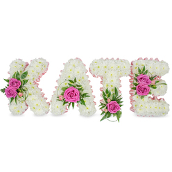 Crafted with quiet care in Highgate, this personalised floral name tribute spells KATE in substantial, freestanding letters made from tightly packed, pristine white chrysanthemums. Each chrysanthemum is set so closely to its neighbour that the letters take on a soft, cloud-like volume, their surfaces almost tactile to the touch. A pale pink satin ribbon delicately outlines the inner curves and negative space of the K, A, T and E, the ribbon's sheen catching light and lending a refined, feminine contour to the structure. Hot pink roses provide dramatic focal points: two gracefully open roses on the K's left section, a single bold rose nestled in the lower centre of the A, another rose placed at the base of the T, and a paired cluster on the right arm of the E. Intermingled greenery - ruscus, slender fern-like fronds and a few variegated leaves - frames those roses and lifts the composition with fresh, gardeny contrast while tiny pink spray blooms and buds soften the edges. The whole arrangement rests against a clean white background, the subtle three-dimensional shadows beneath suggesting a freestanding memorial display. As a florist who regularly prepares tributes for families visiting Highgate Village, Waterlow Park and the cemetery, I find this design reads as both dignified and intimate: the white and pink palette expresses purity, compassion and affection, an eloquent floral farewell that honours memory with gentle craftsmanship. - Flowers Highgate, flowershighgate.mom