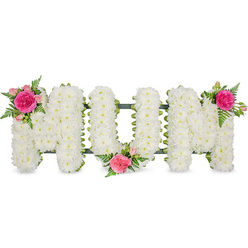 In this image, the word MOM is rendered in large, structured floral letters, arranged in a straight line against a crisp white background. Each letter is thoroughly encrusted with white chrysanthemums or similar small, daisy-like blooms, their petals overlapping so densely that no gaps in the base can be seen. The surface appears soft and almost cushion-like to the touch, yet the edges are clean and precise, reflecting careful floristry work. A narrow dark green frame or backing peeks out at the base of the letters, anchoring the word visually and hinting at the practical support that holds each stem in place. To break the expanse of white, three accent sprays of pink roses and fresh foliage are positioned with a thoughtful sense of balance. On the top-left of the first 'M', a vivid fuchsia garden-style rose sits at the heart of the cluster, surrounded by smaller, paler pink roses and buds. The greenery-slender fern fronds and leafy stems-spills gently around the blooms, giving the design movement and a more natural feel. A second cluster nestles low between the 'O' and the final 'M', while a third crowns the upper right corner of the last letter, guiding the eye lightly from left to right. The overall effect is one of calm, graceful remembrance, combining traditional white funeral flowers with touches of warm pink to honour a mother's love. It is the type of personalised tribute you might see delivered to a service in Highgate, perhaps at a local church off Archway Road, a tender statement crafted to bring a sense of solace to family and friends.
