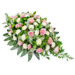 This image shows a refined, elongated funeral spray, beautifully arranged in a soft teardrop silhouette and photographed against a clean, white backdrop to highlight every detail. The design begins with a lush, rounded cluster of soft pink roses at the upper left, gradually narrowing into a delicate point at the right as flowers and foliage taper away. The roses themselves are the stars of the piece, showcasing an array of pink tones from pale blush to mellow rose, each bloom at a slightly different stage - some tightly cupped, others fully opened, revealing layered petals that create a sense of depth and tenderness. Interwoven with the roses are clusters of white carnations and smaller spray carnations. Their ruffled petals bring a gentle, cushion-like texture, brightening the composition and softening the visual transition between blooms and greenery. Around and beneath this floral core lies a generous sweep of foliage. Broad, glossy leaves provide a strong dark green frame, suggesting stability and support, while rounded eucalyptus leaves in soft, silvery-green add cooler accents and a subtle, airy quality. From the narrow, right-hand tip, graceful tendrils of trailing ruscus fall away, their deep green leaves creating a natural cascade that leads the eye along the spray's length, much like a path winding through Waterlow Park. The mood is peaceful and reflective, ideally suited to a memorial service or funeral in the Highgate area. Although silent, the arrangement conveys a message of heartfelt condolences, offering a beautifully balanced, living tribute that honours a loved one's memory with quiet elegance and respect.