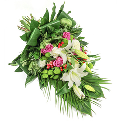 This dynamically flowing diagonal spray is a tapestry of tranquillity and vibrance, reminiscent of a peaceful day in Highgate's verdant spaces. Dominating the ensemble, elegant white lilies-each one a vision of purity-stand amidst unfolding buds and lush greenery, their golden stamens aglow in the light. Pink roses offer rich, layered notes of affection and remembrance, their gentle bloom mirrored by the soft ruffles of white spray carnations tucked amongst the arrangement. Bright green santini chrysanthemums provide a bold, textural highlight, their mossy globes forming lively counterpoints to the surrounding foliage. Small clusters of vivid red hypericum berries punctuate the greens and blushes, drawing one's attention like red berries along the hedgerows lining Highgate Wood. The arrangement's base is built on a foundation of glossy, architecturally folded leaves, trailing palms, and fine, feathered sprigs, giving the bouquet movement and dimension. Light shimmers across the surfaces, elevating each detail and providing a sense of both optimism and peaceful reflection. Crafted for funeral or memorial settings in Highgate, this arrangement delivers a message of warmth and condolence, its considered palette and structured cascade ensuring a fitting tribute for any solemn occasion within the neighbourhood.