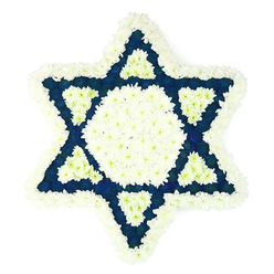 This image showcases a large Star of David funeral arrangement, photographed square-on so the design's symmetry is easy to picture. The star is created entirely from closely packed blooms, primarily in crisp white and a profound dark blue, and is set against a simple white background that keeps all attention on the flowers. A thick edging of fluffy white chrysanthemums outlines the six points, their soft, feathery petals creating a gentle cushion that defines the star's distinctive silhouette. Within this outer frame lies a broad white hexagon at the centre, filled so densely that no gaps are visible, giving the impression of a smooth, calm island of light. Radiating from this centre, six navy triangular panels form the star's points, each one shaped precisely from small-petalled blue flowers that bring a sense of weight, dignity, and depth. At the inner base of every dark blue triangle sits a smaller white triangle, repeating around the design like a quiet heartbeat of light, and creating an intricate pattern that feels carefully thought out rather than decorative alone. The texture of the tribute is rich and velvety; you can almost feel the cool heads of the chrysanthemums and carnations beneath your fingertips, and imagine the faint, fresh scent that would greet you at a Highgate chapel or synagogue. This Star of David piece is unmistakably meant for Jewish funerals and times of mourning, suited to services held around Highgate, Muswell Hill, and Archway. Crafted by an experienced local florist, it offers a respectful way to honour a life, blending symbolism, tradition, and the comforting presence of fresh flowers.