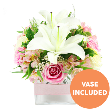 This image presents a beautifully balanced floral arrangement standing out clearly against a pure white backdrop, the design evoking the calm charm of Highgate's leafy lanes and hidden gardens. At the centre of the bouquet, two impressive white Oriental lilies stretch open, their thick, waxy petals arranged like stars, curling slightly at the edges to reveal deep reddish-brown stamens and a soft, creamy base. Surrounding these lilies in a tender embrace are numerous soft pink roses, some tightly furled in bud form, others generously open with rippling layers of petals that catch the light, lending a luxurious, romantic feel. Weaving among the roses and lilies, clusters of pink and white alstroemeria bring a more delicate, elongated shape; their inner petals are brushed with yellow and small speckles, adding fine detail that rewards a closer look. Airy tufts of white baby's breath are scattered throughout the arrangement, floating between blooms like a mist, softening transitions and adding a light, ethereal quality reminiscent of morning fog drifting over Highgate Woods. The flowers rest against a background of lush greenery, including broad, glossy leaves and finer feathery fronds, creating both structure and contrast and suggesting freshness, as if the stems were freshly conditioned by an experienced florist. All are gathered neatly into a modern, square clear glass vase, whose clean lines and transparent sides reveal the straight stems and clear water within. Around the middle of the vase, a pale pink satin ribbon is tied horizontally, the smooth fabric echoing the soft pastel palette of the flowers. In the bottom right corner, a vivid circular orange emblem with bold white capital lettering reads "VASE INCLUDED," clearly indicating that the container is part of the floral gift. The overall impression is one of gentle joy and refined elegance, an ideal centrepiece for intimate celebrations, quiet dinners, or same-day delivery around Highgate and nearby streets.