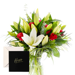 Elegance and emotion meet in this bouquet, a portrait of Highgate's refined spirit. The white lilies rise center stage, their large trumpet blossoms gleaming in bright, clear light, petals creamy and smooth as satin, their scent clean with a hint of spice settling like memory. Red roses cluster through the arrangement, their velvety depth weaving among the lilies, a warm thread through the composition. Surrounding them, abundant green spears and curling foliage create a living frame, emerald leaves catching and holding the glow of daylight. Unopened buds promise future beauty, like opportunities yet to unfold in a life well tended. The bouquet sits in a simple glass vase, unassuming, allowing every stem to tell its part of the story. It feels both sophisticated and comforting, a thoughtful gesture for someone whose example inspires others - a mentor, friend, or hero - and a whispered assurance that their strength is seen. The accompanying card, marked Hero, heightens the moment with a personal note of gratitude or remembrance. Delivered with same-day service to homes or workplaces across Highgate and surrounding postcodes, the freshness and fragrant balance will speak for itself. Close to Waterlow Park and the Heath, this arrangement travels easily to neighbours in Crouch End and Muswell Hill, making it ideal for a thank-you, a remembrance, or a quiet celebration of achievement. A gift that nods to courage and resilience, it leaves a lasting impression of warmth and respect.