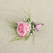 On a softly textured background of light beige fabric, reminiscent of natural linen laid across a Highgate studio counter, a meticulously crafted pink rose boutonniere is displayed with quiet poise. The rose is placed at a gentle diagonal in the lower left of the image, its petals unfurling in a tight, elegant spiral. The colour transitions from a pale, baby pink at the centre to richer fuchsia and magenta hues along the outer edges, giving the flower an ombré effect that feels both classic and contemporary. Encircling the rose, clusters of tiny white baby's breath lend a weightless, cloud-like finish, their minute blossoms softening the overall look and adding an almost bridal delicacy, ideal for ceremonies in Highgate's churches or nearby registry offices. Wisps of slender, grass-like greenery reach out from behind the main bloom, some strands arching upward while others rest gently along the fabric, providing a sense of organic flow and natural texture. At the base, a broader leaf in deep emerald green has been expertly curled into a supportive collar, its smooth surface glistening with a few scattered droplets of water, suggesting recent hydration and attentive preparation. The stems of the rose and foliage are bound together by a pale pink satin ribbon, tightly and evenly wrapped to create a tidy, polished handle, finished with a neat bow in a deeper magenta shade that echoes the rose's outer petals. The neutral, uncluttered backdrop ensures the focus remains on the interplay of pinks, greens, and whites, making this boutonniere a tasteful accent for grooms, ushers, or prom guests celebrating in and around Highgate.