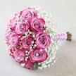 Delicately arranged and exuding a joyful sophistication, this classic round bouquet rests against a softly toned fabric backdrop evocative of Highgate's graceful interiors. At its core, around a dozen vibrant roses reveal petals shaded from gentle, dusty pink-lavender at the centre to brilliant fuchsia along the edges, each bloom fresh and expressive. Airy clusters of white baby's breath float between the roses, lending a dreamy, cloud-like dimension that highlights the arrangement's romance and lightness-calling to mind Highgate's serene gardens. The stems are neatly assembled and tightly wrapped with a silky blush-pink ribbon, which is elegantly twined with a pearl strand to evoke a sense of local refinement and tradition. Slightly visible natural stem ends underscore the bouquet's authenticity and freshness, as valued by same-day delivery customers across Highgate and Archway. The bouquet's even, soft lighting accentuates dewdrops on the petals and the intricate ballet of blooms, making this arrangement a fitting choice for those moments in Highgate life that deserve celebration-weddings, anniversaries, or simply a heartfelt gesture from Flowers Highgate.