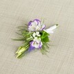 A delicately crafted wedding boutonniere rests on a softly textured light beige linen cloth, the neutral background allowing every petal and stem to stand out with quiet confidence. At the heart of the design are two white lisianthus blooms, their petals luxuriously ruffled and finely edged with deep, velvety purple, creating a striking bi-colour halo that feels both modern and timeless. Nestled between them are dainty clusters of tiny white filler flowers, much like baby's breath, which add a light, cloud-soft texture and a gentle sense of romance. A slender vertical spike of grape-hyacinth-like blossoms, in rich purple-blue tones, rises through the composition, its tiny bell-shaped florets giving an intriguing architectural line. Around these focal flowers, fine feathery greenery, reminiscent of asparagus fern, mingles with slightly broader green leaves, offering contrast, movement, and the sense of something freshly gathered from a Highgate garden after early morning rain. Two pale green unopened buds peek out from the cluster, suggesting new beginnings and the unfolding of a special day. All the stems are neatly aligned and wrapped in a smooth white satin ribbon, tied with a small, precise bow that marks this piece as ready for a lapel-perhaps for a groom walking through Waterlow Park for photos, or a prom guest arriving from near Highgate Village. The lighting is soft and even, highlighting the crisp whites, saturated purples, and fresh greens, and the overall feeling is one of understated elegance and thoughtful craftsmanship, just as you might expect from a seasoned local florist preparing flowers for an intimate North London celebration.