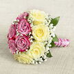 Captured from above on a neutral, woven background that resembles natural linen in warm off-white, this hand-tied rose bouquet feels as if it has just been set down in a light-filled Highgate townhouse. The arrangement forms a rounded, almost medallion-like shape, with two colour fields of roses that meet gracefully in the middle. On one side, rich fuchsia and magenta-pink roses spiral open, their petals velvety and precise, while the opposite side is filled with soft, creamy yellow roses that bring a light, buttery glow. Interspersed throughout, tiny white sprays of baby's breath create a delicate, airy cloud that bridges the two colours, like a gentle haze over nearby Waterlow Park on an early morning. A handful of dark-green leaves peep out around the edges and between blooms, providing subtle structure and a whisper of garden freshness. The stems beneath are neatly aligned and secured into a compact handle, wrapped tightly with lustrous pink satin ribbon that has a gentle shimmer when the light hits. Over this satin, a slender string of white pearls spirals down the handle, adding an elegant, bridal detail with the quiet charm of something borrowed and cherished. The mood is one of poised romance and timeless taste, echoing the understated luxury often associated with Highgate weddings and celebrations. Whether carried down the aisle at a local ceremony, placed as a centrepiece at an intimate gathering, or used in online features about wedding flowers and rose symbolism, this bouquet visually expresses affection, commitment, and the craftsmanship of a skilled North London florist.