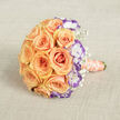 Laid gently across a woven, light beige fabric background and viewed from slightly above, this bridal bouquet exudes a hush of affection and deliberate elegance. The central cluster is a full, rounded gathering of peach and soft orange roses, each petal curling with a plush, tactile richness that promises the warm, heady scent of freshly cut garden roses. Interspersed among them are white lisianthus with striking violet-edged petals; their crisp white interiors and deep purple rims bring a cool, sculptural contrast that modernises the classic palette. Feather-like sprays of gypsophila drift between blooms, introducing an ethereal, almost powdery lightness that balances the composition. The handle is wrapped in pale peach satin, the fabric's sheen catching highlights, while a string of cream pearls wraps around the ribbon in an elegant spiral-details that feel ceremonial and intimately handcrafted. The photograph's soft lighting softens shadows and reveals subtle gradients across each bloom, much like the diffused daylight in Highgate near the Victorian terraces and tree-lined lanes. This bouquet reads as quietly celebratory and tender, suited to a wedding procession through Highgate Village or an intimate ceremony in a nearby church hall. The arrangement communicates careful craftsmanship and emotional warmth: a floral embrace that pairs tradition with a touch of contemporary sophistication, ready to be held close as vows are spoken or promises renewed.