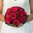 Bathed in natural daylight just steps from the Highgate woods, this photo portrays a bride clasping a bouquet radiant with bold romance and textural intrigue. Velvety, ruby red roses-with petals in mesmerising swirls from opening buds to full blossoms-anchor the compact arrangement. Bright clusters of scarlet hypericum berries peek playfully between roses, their sheen catching the light like tiny gemstones. Encircled by broad, deep green leaves, the bouquet takes on a sculpted, elegant shape that echoes the leafy landscape of North Road and the surrounding parks. The bride, enveloped in the subtle sophistication of a white gown adorned with lace, holds the bouquet close-her hands manicured, her stance one of joy and anticipation. The lighting, soft and even, heightens the bouquet's rich textures and hues, inviting the senses to imagine its velvety touch and gentle, sweet fragrance. This arrangement, designed in Highgate's floristry tradition, channels the excitement and rooted beauty of a North London wedding, echoing the area's legacy of artistry and celebration.