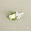 Laid across a neutral, lightly textured cream-beige weave, this boutonniere presents a composed, classic silhouette that feels at once tailored and intimate. The focal point is a single ivory rosebud, its petals compact and velvety, unfolding inward with a calm, deliberate symmetry that suggests careful selection by an experienced hand. Around it, tiny clusters of baby's breath - immaculate white gypsophila - form a soft cloud, their minuscule blossoms acting like a luminous frame against the rose's creamy skin. The arrangement's greenery brings contrast and character: fine, feathery sprigs of deep green that recall cedar or evergreen add a subtle, resinous suggestion, while larger, glossy leaves create weight and balance beneath the bloom.
A smooth white satin ribbon binds the stems, tied in a modest bow at the base; the ribbon's sheen and clean finish read as ceremonial and refined without excess. Close to the lapel, this boutonniere whispers rather than shouts, ideal for a groom or groomsman exchanging vows in Highgate's historic lanes or pausing for photos beside the elm-lined paths of Highgate Wood. The scent is delicate - a soft, clean floral note that evokes early spring mornings - and the tactile contrast between velvety petals, airy gypsophila and crisp foliage is immediately pleasant to the touch. As a local florist we at Flowers Highgate would note the piece's versatility: it complements muted tailoring, cream or navy jackets, and suits intimate ceremonies in village chapels or elegant gatherings near Archway. The neutral fabric beneath highlights every contour and shade, making this boutonniere easy to coordinate with stationery and portrait lighting.
